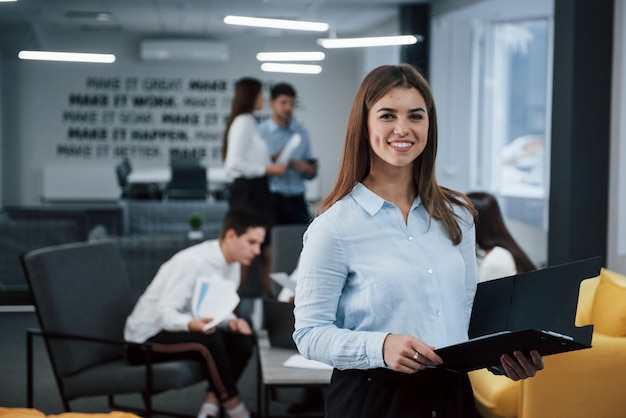 Belle femme joyeuse. Portrait de jeune fille se tient dans le bureau avec des employés à l'arrière-plan