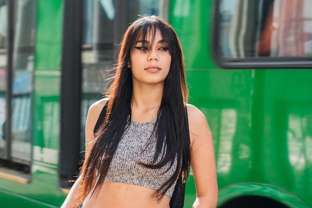 une belle femme latina à la peau foncée, debout dans la rue en attendant les transports en commun, à côté d'elle passe un bus vert (méga bus). une étudiante sur le chemin de la classe. concept de liberté.