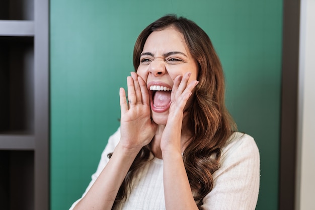 Belle femme latine criant fort à côté avec la main sur la bouche. Notion de communication.