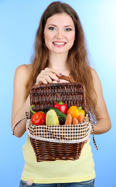 Belle femme avec des légumes dans un panier en osier sur fond bleu