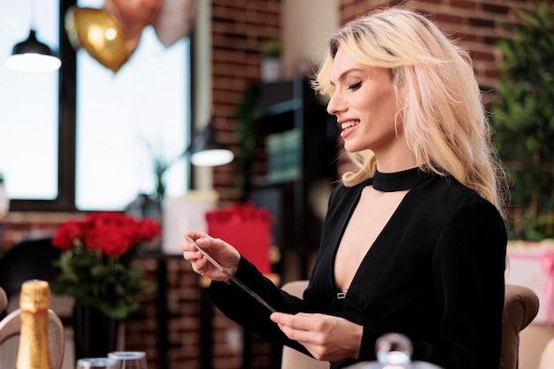 Belle femme lisant la carte de voeux romantique de la Saint-Valentin, assise dans le salon avec des cadeaux coûteux. Jolie fille blonde avec des cadeaux de luxe, 14 février surprises romantiques