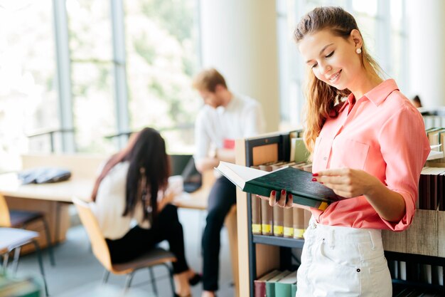 Belle femme lisant un livre dans une bibliothèque et pensant