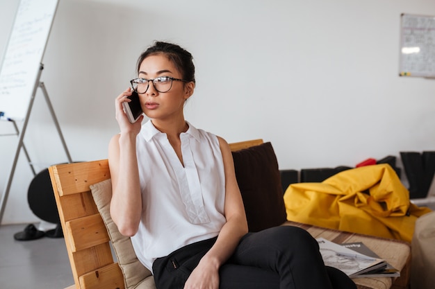 Belle femme à lunettes assis et parlant sur téléphone mobile