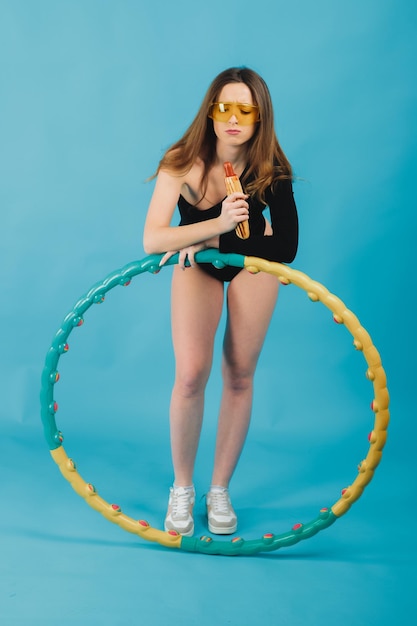 belle femme à lunettes jaunes avec un hula hoop tient un hot-dog dans sa main