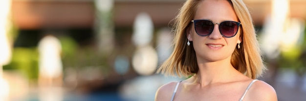 Belle femme à lunettes de soleil et robe sur fond de piscine à l'hôtel en été.