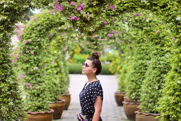 Belle femme à lunettes de soleil se tient sous des arches couvertes de fleurs