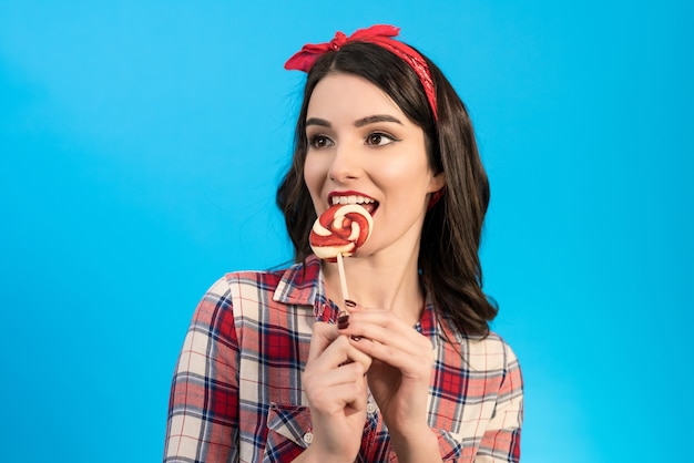 La belle femme mangeant un bonbon sur le fond bleu