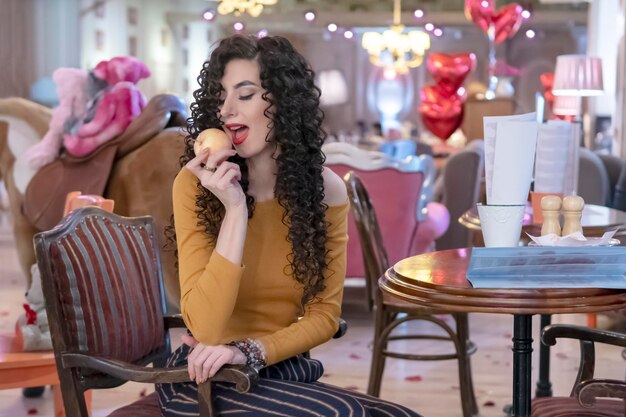 belle femme mangeant une pomme assise à une table dans un café