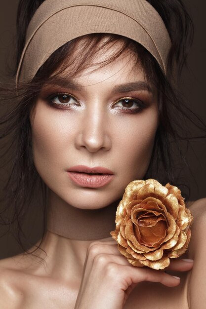 Belle femme avec un maquillage lumineux et une peau parfaite avec des fleurs d'or à la main