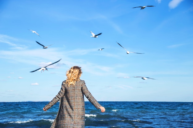 Belle femme marche en automne et pratique la pleine conscience au bord de la mer avec des mouettes.