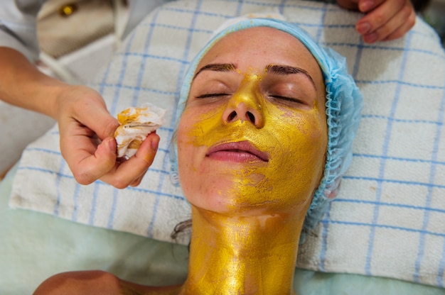 Belle femme avec masque doré du visage au salon de beauté