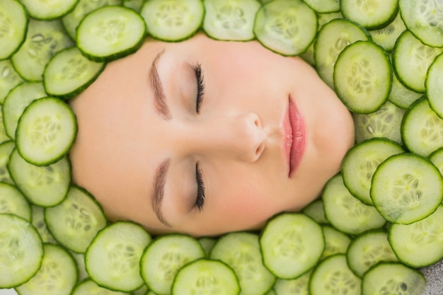 Belle femme avec un masque facial de tranches de concombre sur le visage