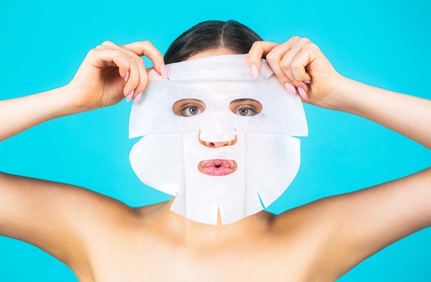 Belle femme avec masque Fille prenant soin du teint de la peau Concept de soins de la peau et de beauté Masque hydratant Femme appliquant un masque en feuille sur son visage sur fond bleu