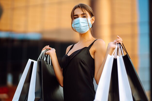 Belle femme en masque médical stérile protecteur avec des sacs à provisions près du centre commercial.