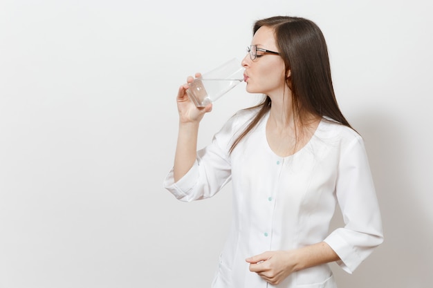 Belle femme médecin confiante isolée sur fond blanc. Femme médecin en robe médicale buvant de l'eau en verre. Personnel de santé, santé, concept de médecine. Copiez l'espace pour la publicité.