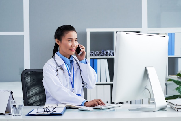 Belle femme médecin généraliste souriante parlant au téléphone avec un patient lors de la vérification des résultats de ...