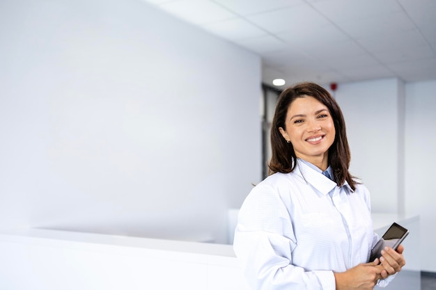 une belle femme médecin souriante debout dans le hall de l'hôpital et tenant une tablette numérique