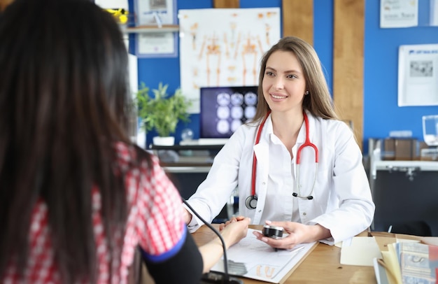 Belle femme médecin travaillant avec un patient mesure la tension artérielle Le médecin utilise un tonomètre pour mesurer la tension artérielle d'une jeune femme et prend des notes