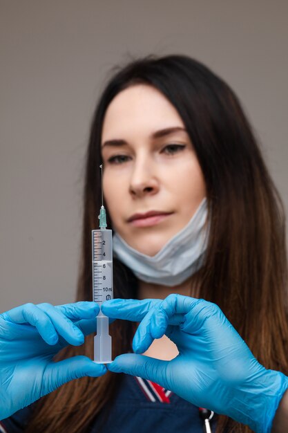 Belle femme médecin en vêtements médicaux blancs, masque, gants bleus et phonendoscope sur ses épaules isolé sur un espace bleu