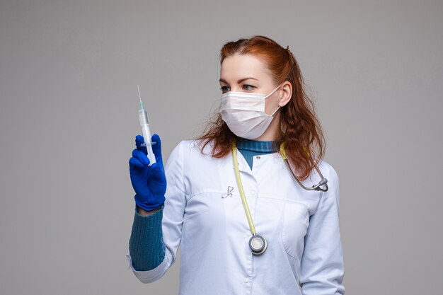 Belle femme médecin en vêtements médicaux blancs, masque, gants bleus et phonendoscope sur ses épaules, photo isolée