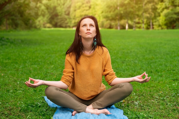 Une belle femme médite assis sur l'herbe verte dans le parc