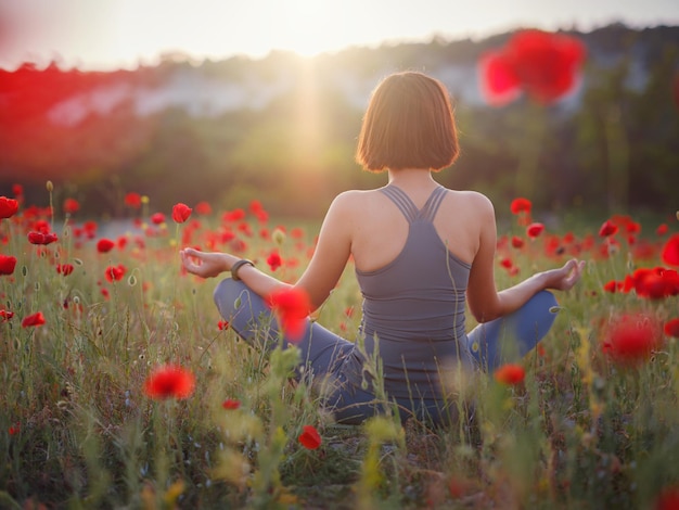 Une belle femme médite sur un champ de pavot au coucher du soleil