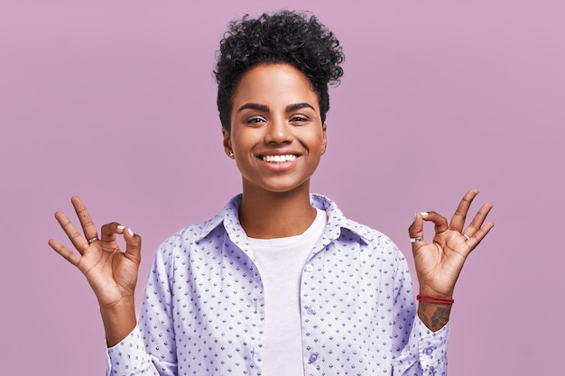 Belle femme métisse avec une coiffure afro, démontre un signe d'accord, étant satisfaite du nouveau projet isolé sur fond lavande. Ethnicité, concept de langage corporel