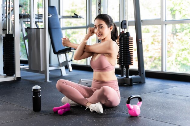 Belle femme mince de remise en forme en vêtements de sport étirant son bras dans une salle de gym, corps mince de fille sexy asiatique - mode de vie Concept de remise en forme de femme en bonne santé