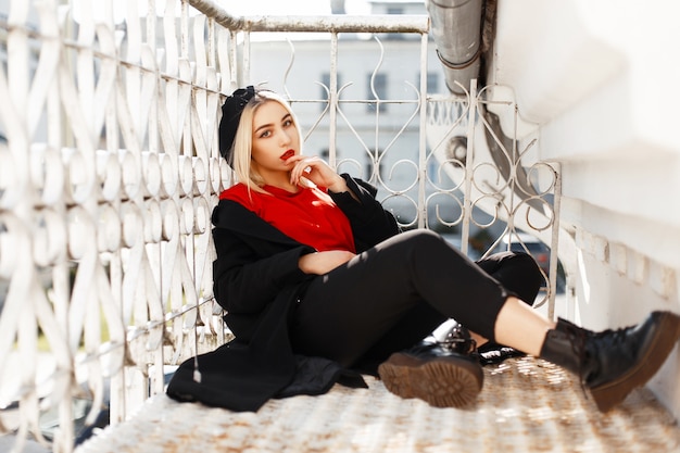 Belle femme à la mode avec des lèvres rouges dans un élégant manteau noir et béret avec des chaussures se trouve dans la rue