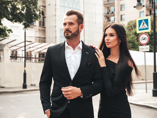 Belle femme de mode et son beau petit ami élégant en costume Modèle brune sexy en robe de soirée noire Couple à la mode posant dans la rue en Europe Homme brutal et sa femme à l'extérieur