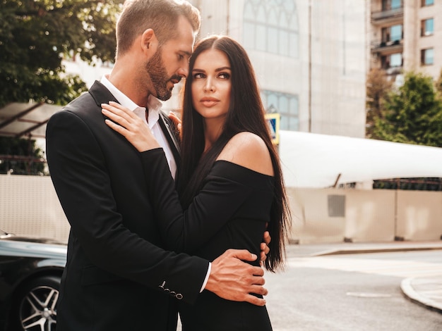 Belle femme de mode et son beau petit ami élégant en costume Modèle brune sexy en robe de soirée noire Couple à la mode posant dans la rue en Europe Homme brutal et sa femme à l'extérieur