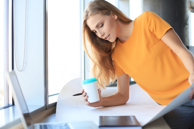 Belle femme moderne écrit quelque chose sur le plan tout en travaillant dans le bureau de création.