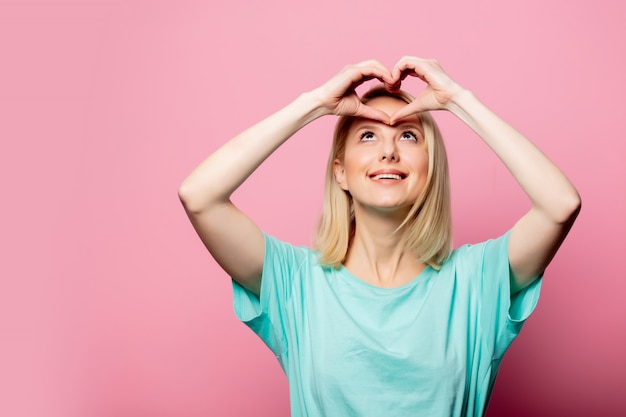 Belle femme montre le geste d'amour sur le mur rose