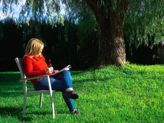 Belle femme mûre appréciant un midi ensoleillé d'hiver dehors lisant un livre dans le jardin