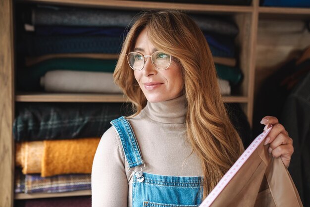 belle femme mûre couturière souriante et travaillant avec du textile à l'atelier