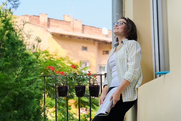 Belle femme mûre dans des vêtements à la maison sur le magazine de lecture de balcon ouvert, espace copie