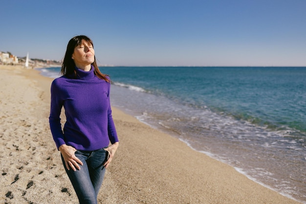 Belle femme mûre se relaxant en respirant de l'air frais par une journée d'hiver ensoleillée à la plage