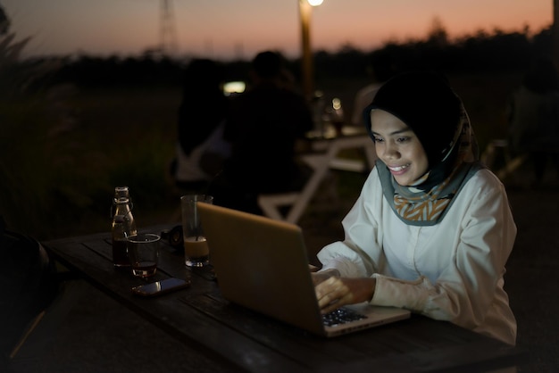 Belle femme musulmane asiatique tenue décontractée travaillant à l'aide d'un ordinateur portable la nuit