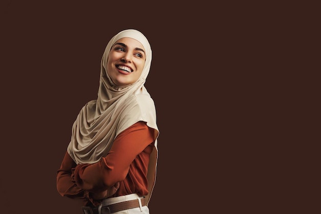 Belle femme musulmane portant un chemisier orange hijab beige et un pantalon beige souriant et regardant