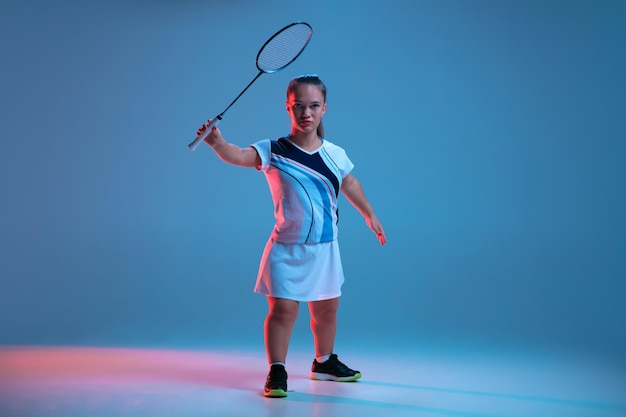 Belle femme naine pratiquant le badminton isolé sur fond bleu à la lumière du néon