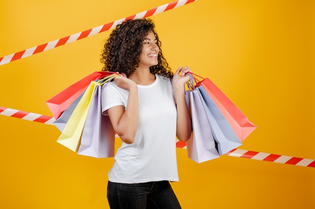 Belle femme noire africaine avec des sacs à provisions colorés isolé sur jaune avec du ruban de signalisation