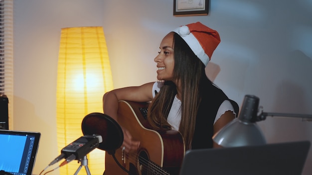 Belle femme noire en bonnet de Noel chantant et jouant de la guitare la veille de Noël