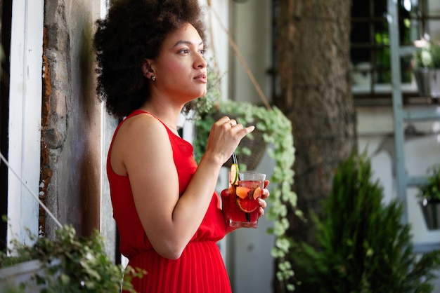 Belle femme noire buvant une boisson saine et souriante en plein air