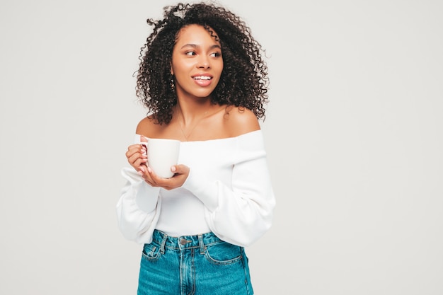 Belle femme noire avec une coiffure de boucles afro. Modèle souriant en pull et vêtements jeans à la mode