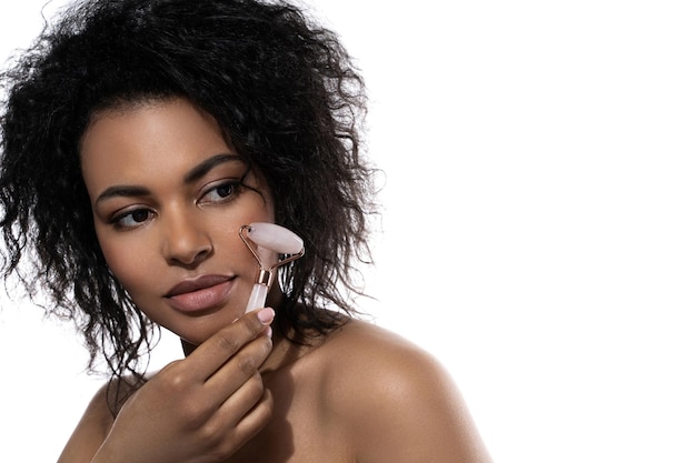 Belle femme noire avec une peau lisse à l'aide d'un rouleau derma quartz rose sur fond blanc