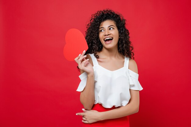 Belle femme noire souriante avec carte de Saint Valentin en forme de coeur isolé sur rouge