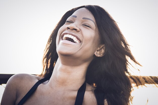 Photo belle femme noire souriante joyeusement - femme caribéenne souriante - longs cheveux noirs lâches - soleil derrière son dos - photo portrait