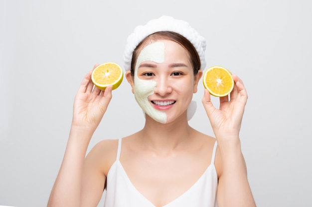 Belle femme obtient un masque d'argile pour le visage et tient des morceaux d'orange sur fond blanc. Concept de beauté, soins du corps et spa