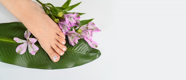 Belle femme parfaite peau jambes pieds vue de dessus avec des fleurs tropicales et feuille de palmier vert