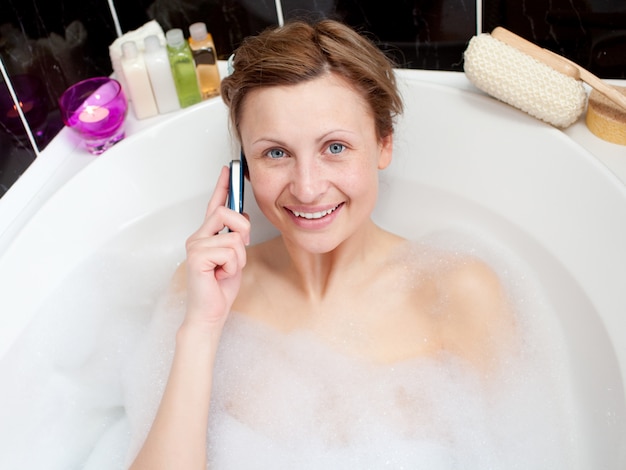 Belle femme parlant au téléphone dans un bain moussant